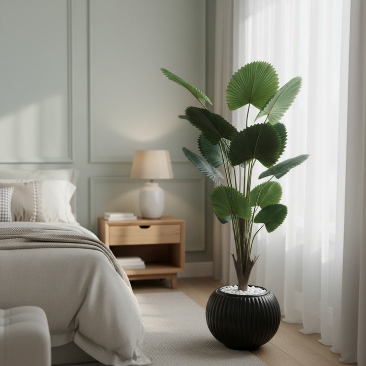 Wadi Home artificial fan palm plant with deep green leaves in a ribbed black planter with white stones in a bedroom.