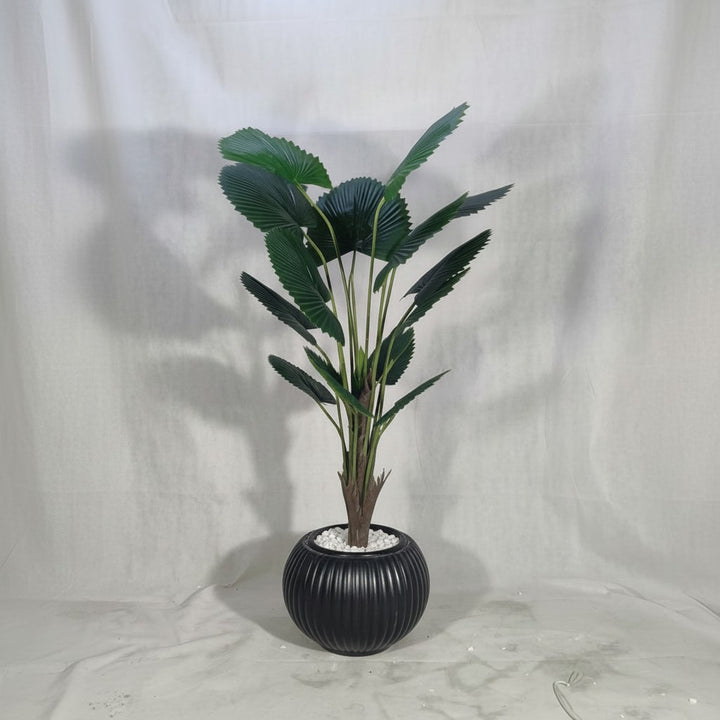 Wadi Home artificial fan palm plant with deep green leaves in a ribbed black ceramic-style pot with white stones.
