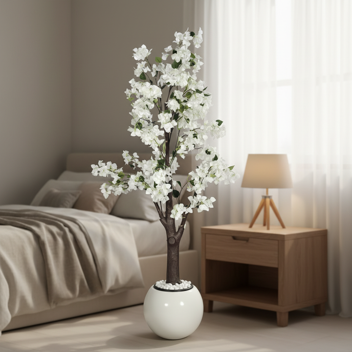 Wadi Home artificial flowering tree with white blossoms and green leaves in a modern white spherical pot in a bedroom.