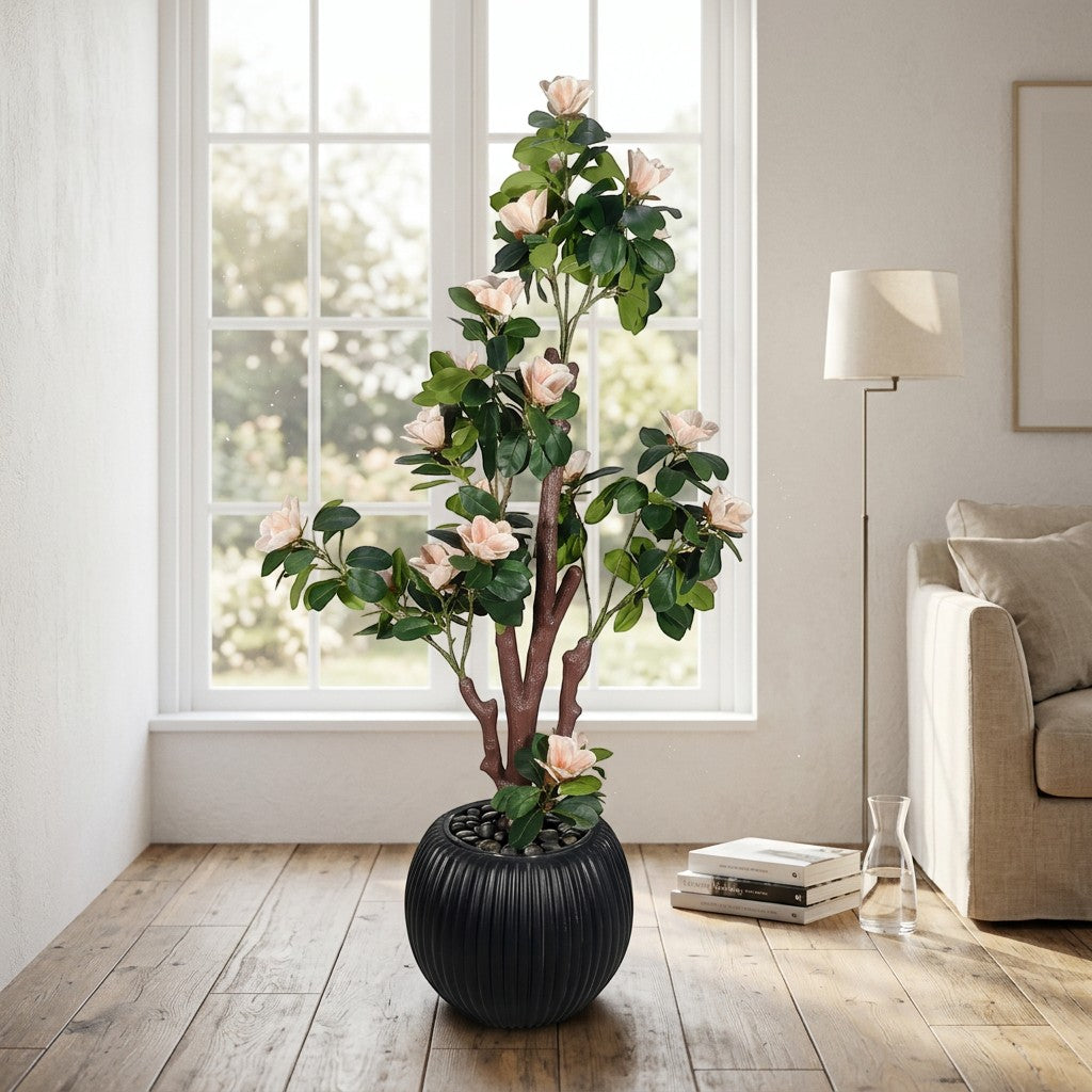 Wadi Home artificial magnolia tree with blush pink blossoms and green leaves in a black textured pot with river stones.