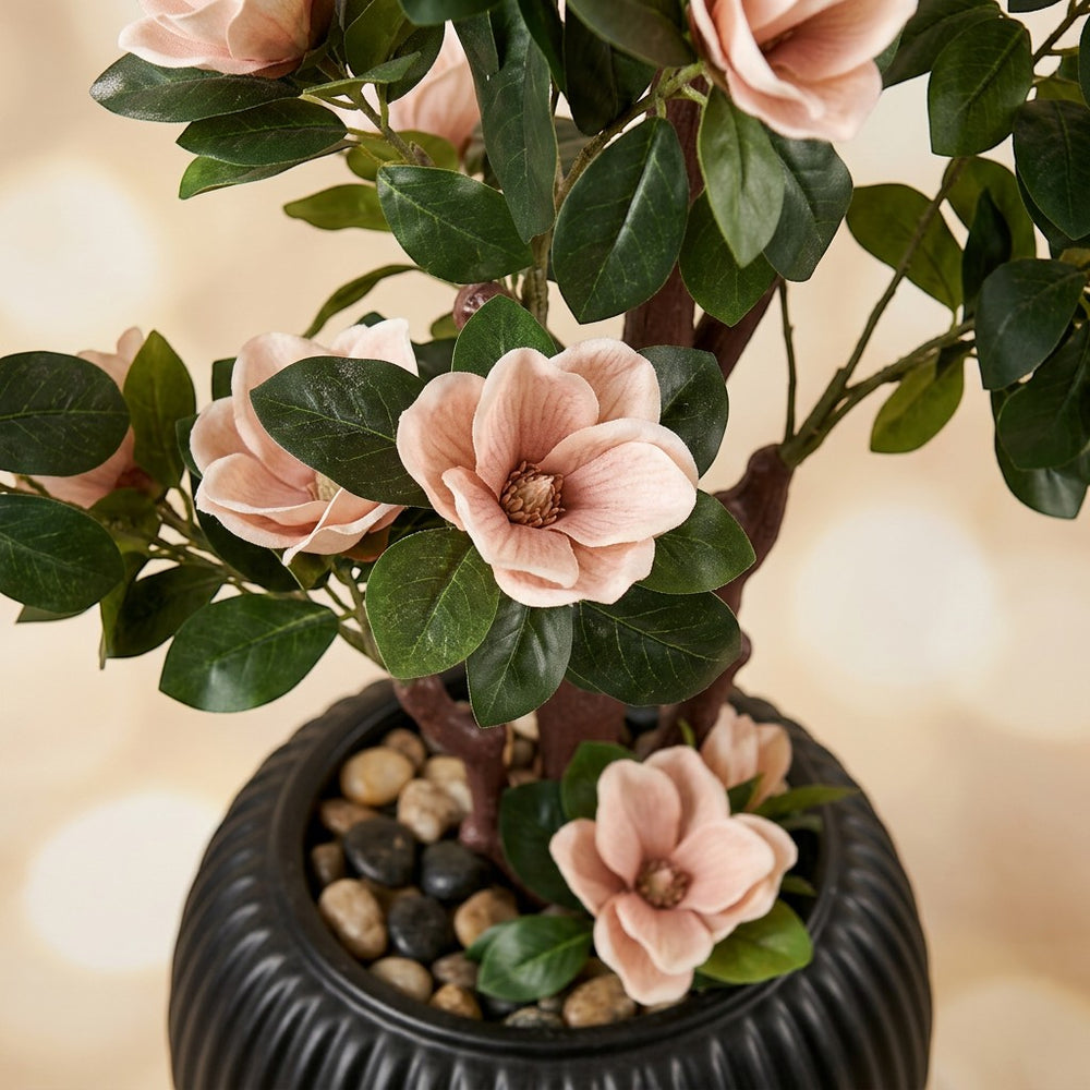 Wadi Home artificial magnolia tree with blush pink blossoms and green leaves in a black textured pot with river stones.