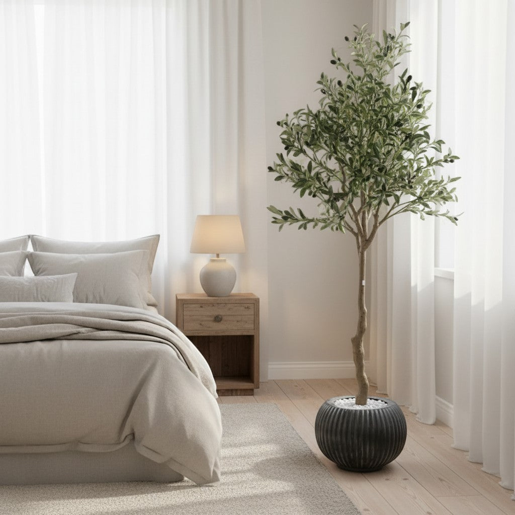 Wadi Home artificial olive tree with green leaves in a ribbed black pot, placed in a modern neutral bedroom.