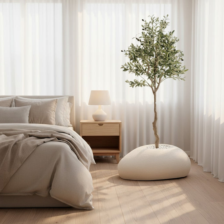 Wadi Home artificial olive tree with green leaves and dark olives in a white stone planter inside a bright bedroom.