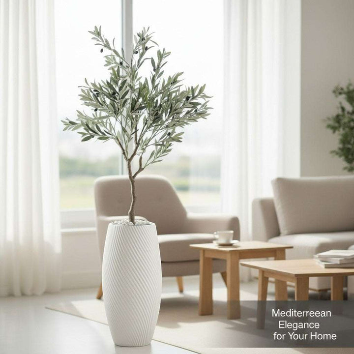Wadi Home artificial olive tree with green leaves and black olives in a white textured planter, styled in a living room.