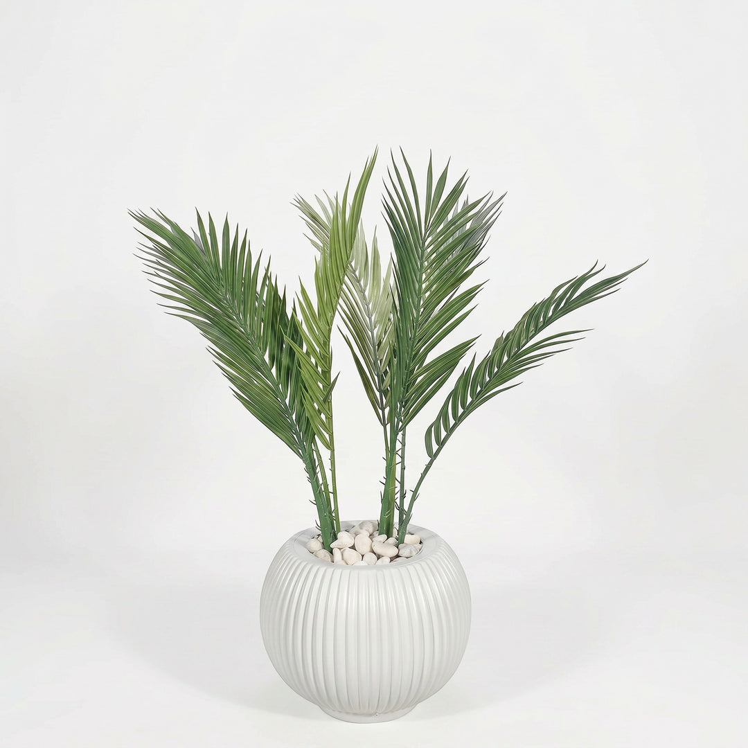 Wadi Home artificial palm plant in a white fluted spherical pot with white pebbles. Lush green fronds.