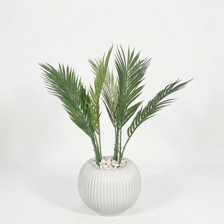 Wadi Home artificial palm plant in a white fluted spherical pot with white pebbles. Lush green fronds.