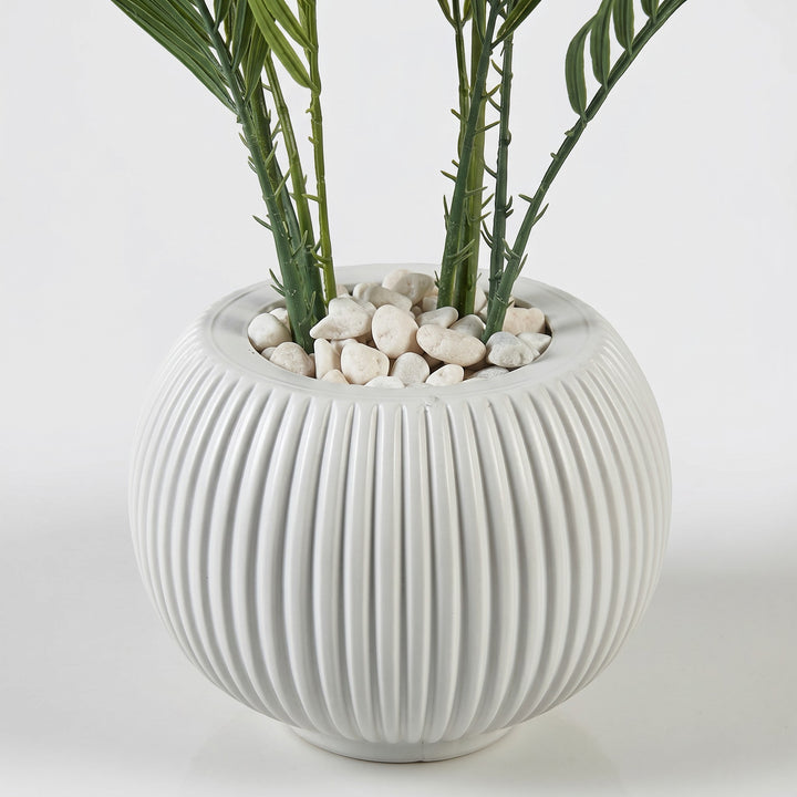 Wadi Home artificial palm plant in a white fluted spherical pot with white pebbles.
