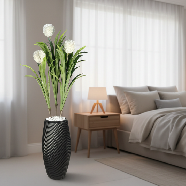 Wadi Home artificial plant with white spherical blooms and green leaves in a black textured spiral vase in a bedroom.