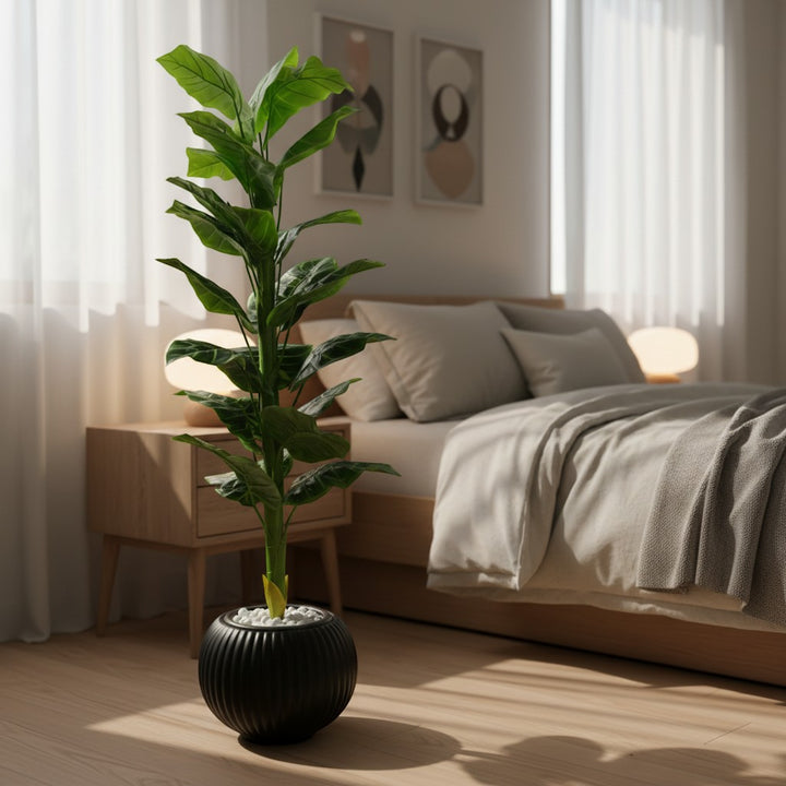 Wadi Home artificial floor plant with vibrant green leaves in a ribbed black pot with white stones in a bedroom.