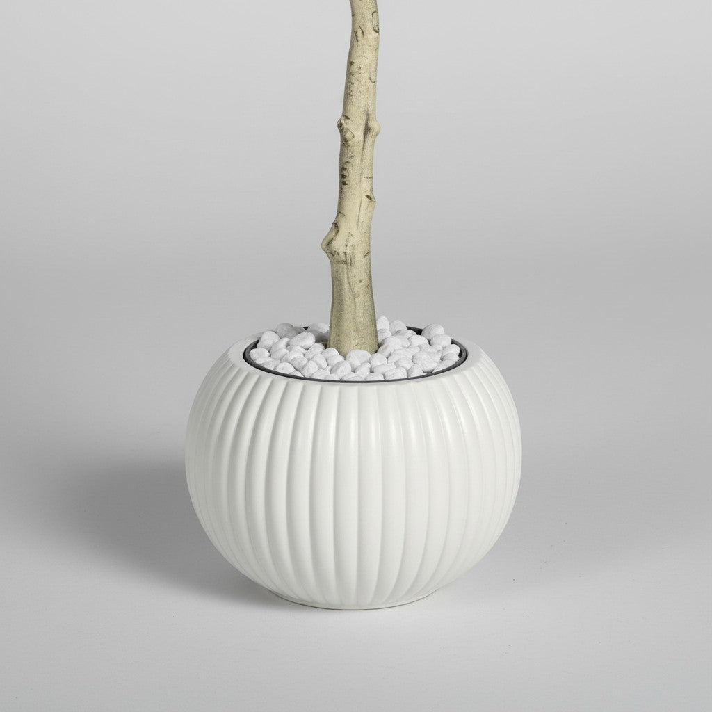 Wadi Home artificial tree trunk in a round ribbed white ceramic pot topped with decorative white pebbles.