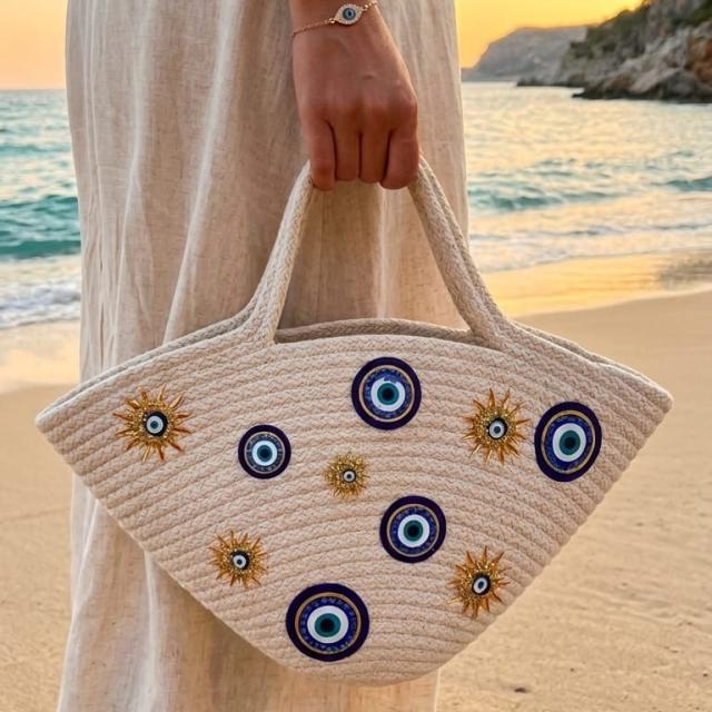 Wadi Home beige rope tote handbag with evil-eye and sun embellishments held by a woman on a beach at sunset.