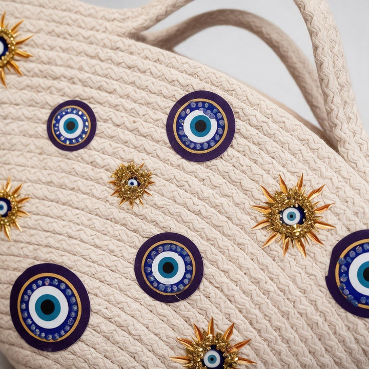 Wadi Home beige rope tote handbag featuring blue evil eye motifs and gold sun-inspired embellishments