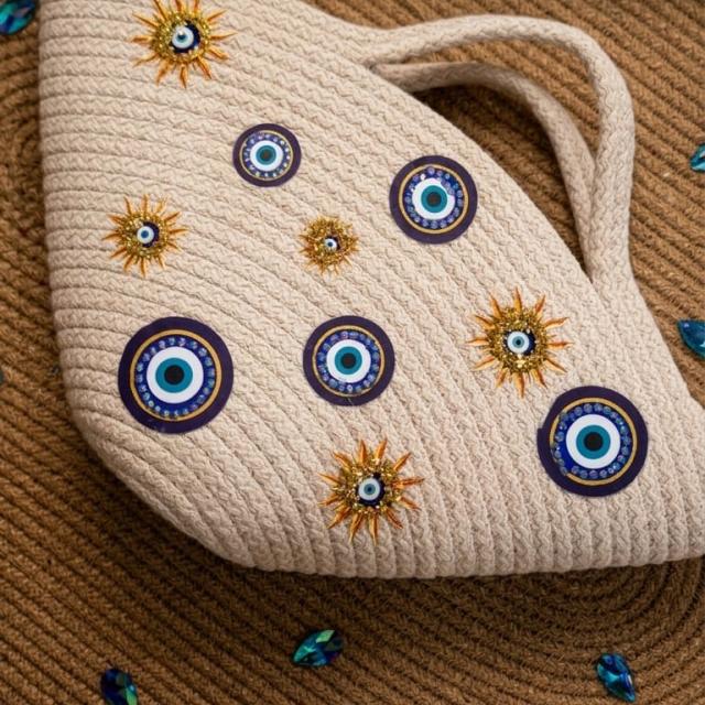 Wadi Home beige rope tote handbag featuring evil-eye motifs and gold sun-inspired embellishments in a semi-circle shape