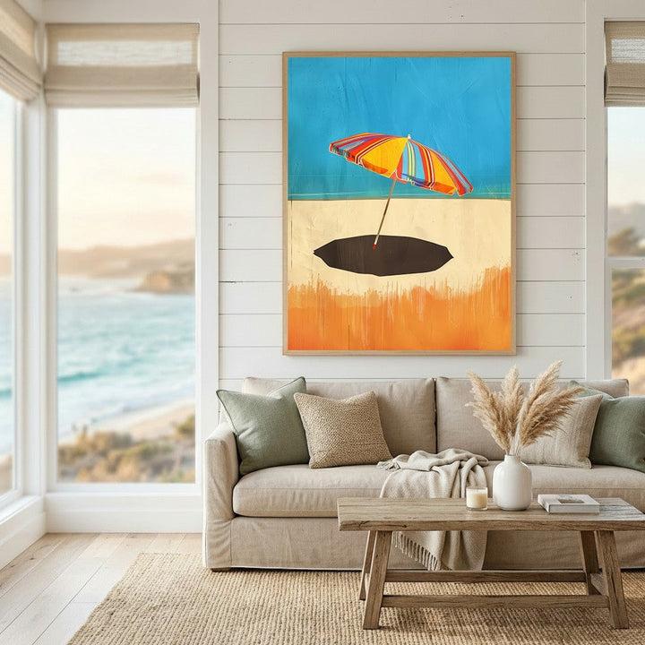 Wadi Home framed wall art featuring a vibrant striped beach umbrella on a sandy shore, displayed above a neutral sofa.