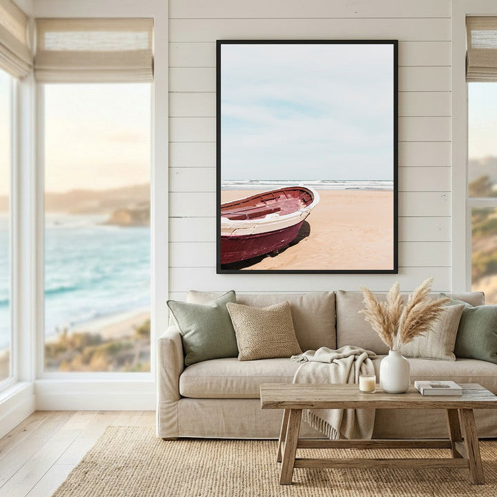 Wadi Home framed coastal wall art featuring a red boat on a sandy beach, displayed above a beige living room sofa.