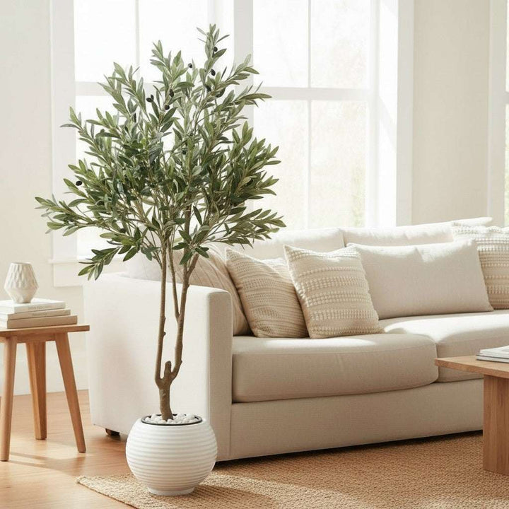 Wadi Home faux olive tree with realistic green leaves and black olives in a textured white pot, placed in a bright living room.