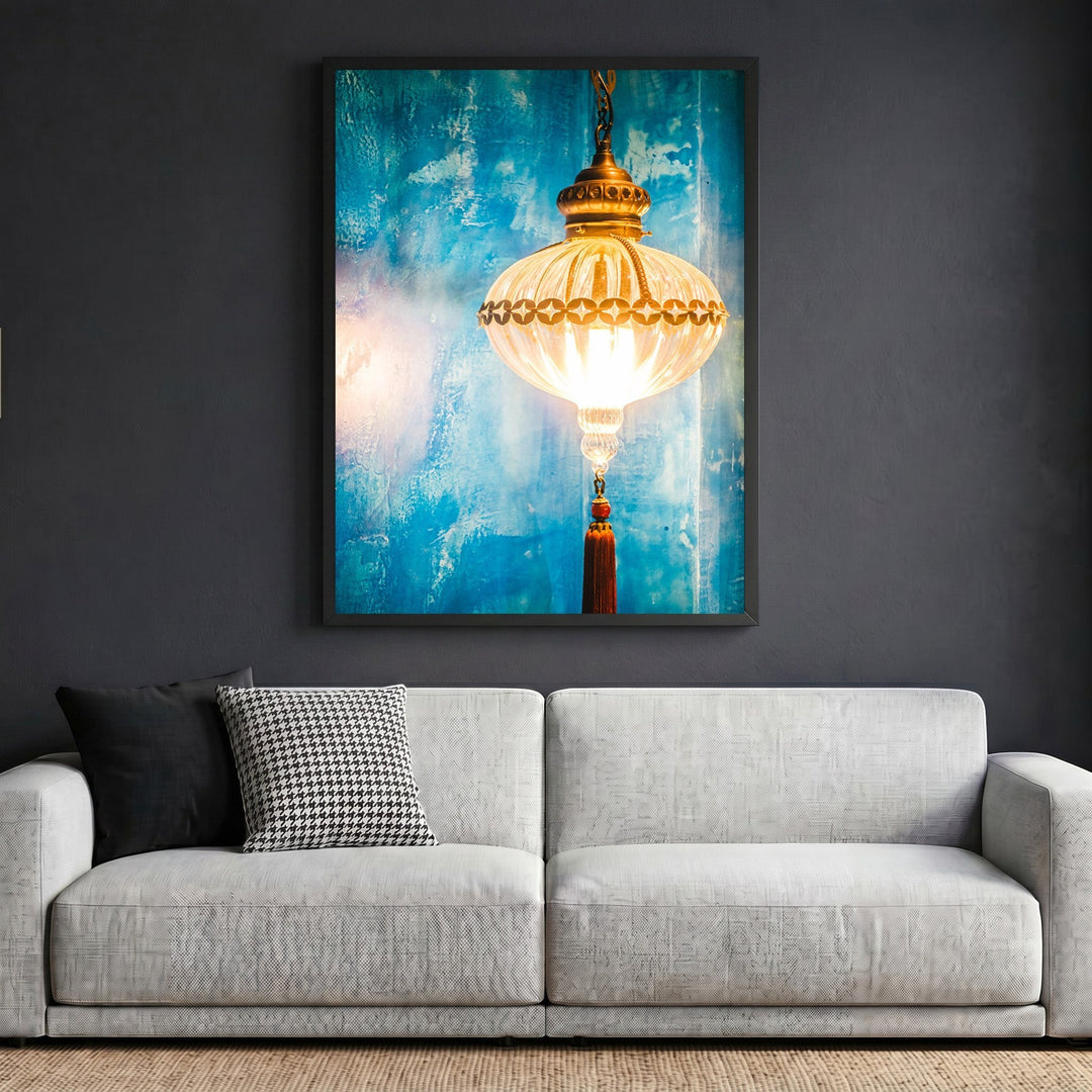Wadi Home wall art print featuring a glowing lantern with a tassel against a textured blue background above a sofa.