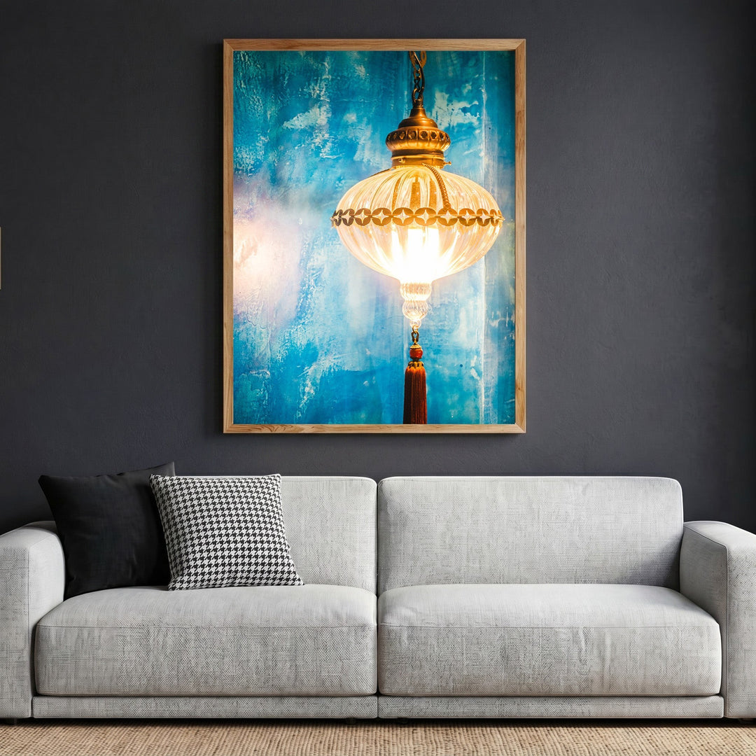Wadi Home framed wall art print of a glowing lantern with a tassel against a textured blue background above a sofa.