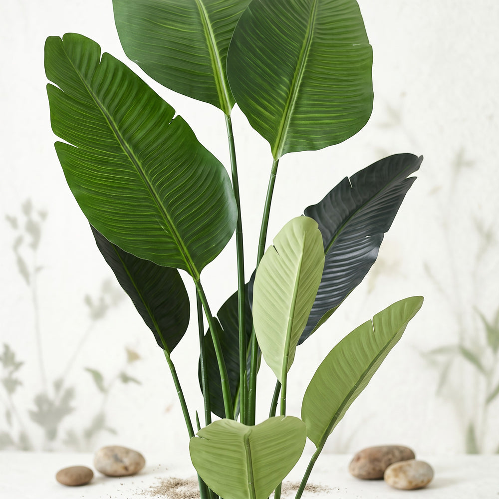 Wadi Home Large Bird of Paradise artificial plant with lush green leaves in a white pot with decorative stones.