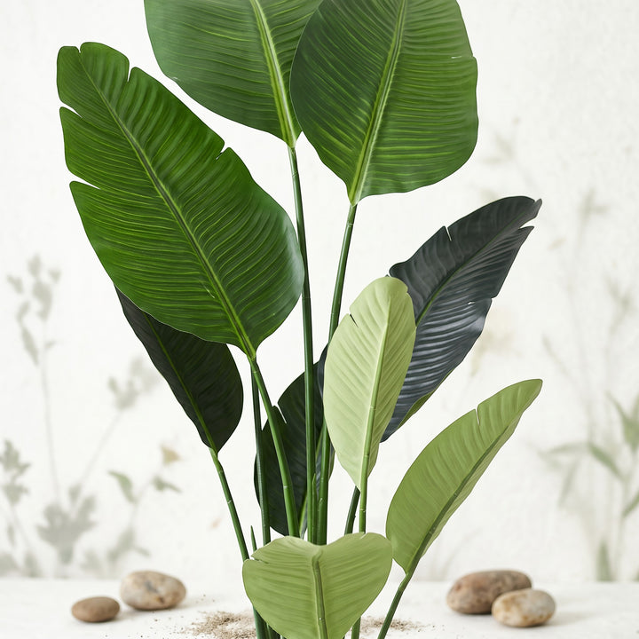 Wadi Home Large Bird of Paradise artificial plant with lush green leaves in a white pot with decorative stones.