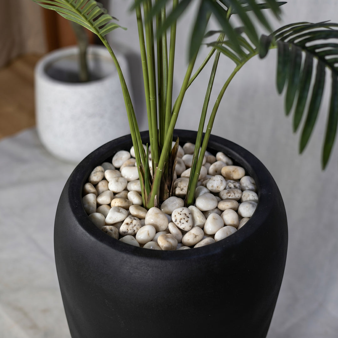 Wadi Home Large Faux Areca Palm Plant in a tall black planter with white river stones and lush green fronds.