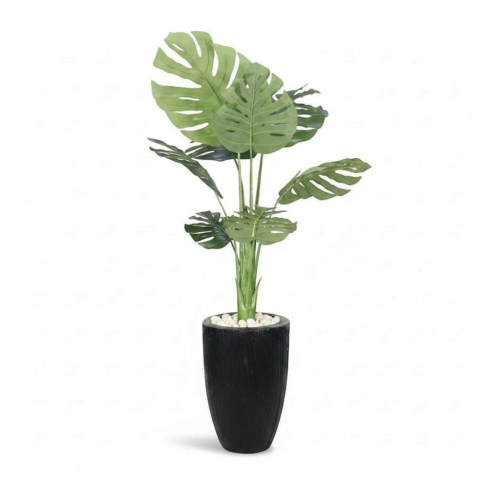 Wadi Home large artificial Monstera plant with split green leaves in a textured black pot with white stones.