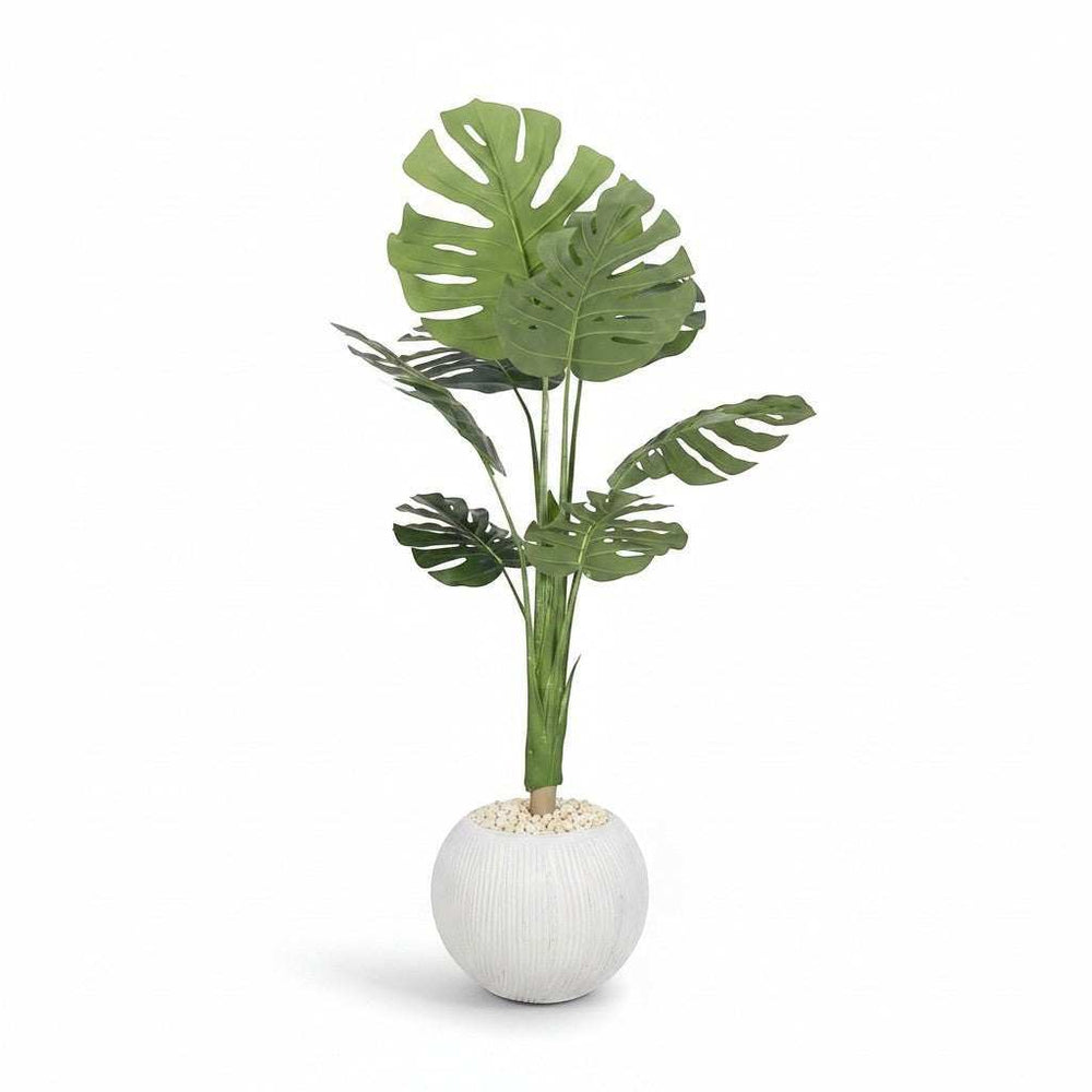 Wadi Home large artificial Monstera plant with deep green split leaves in a textured white spherical pot with decorative stones.