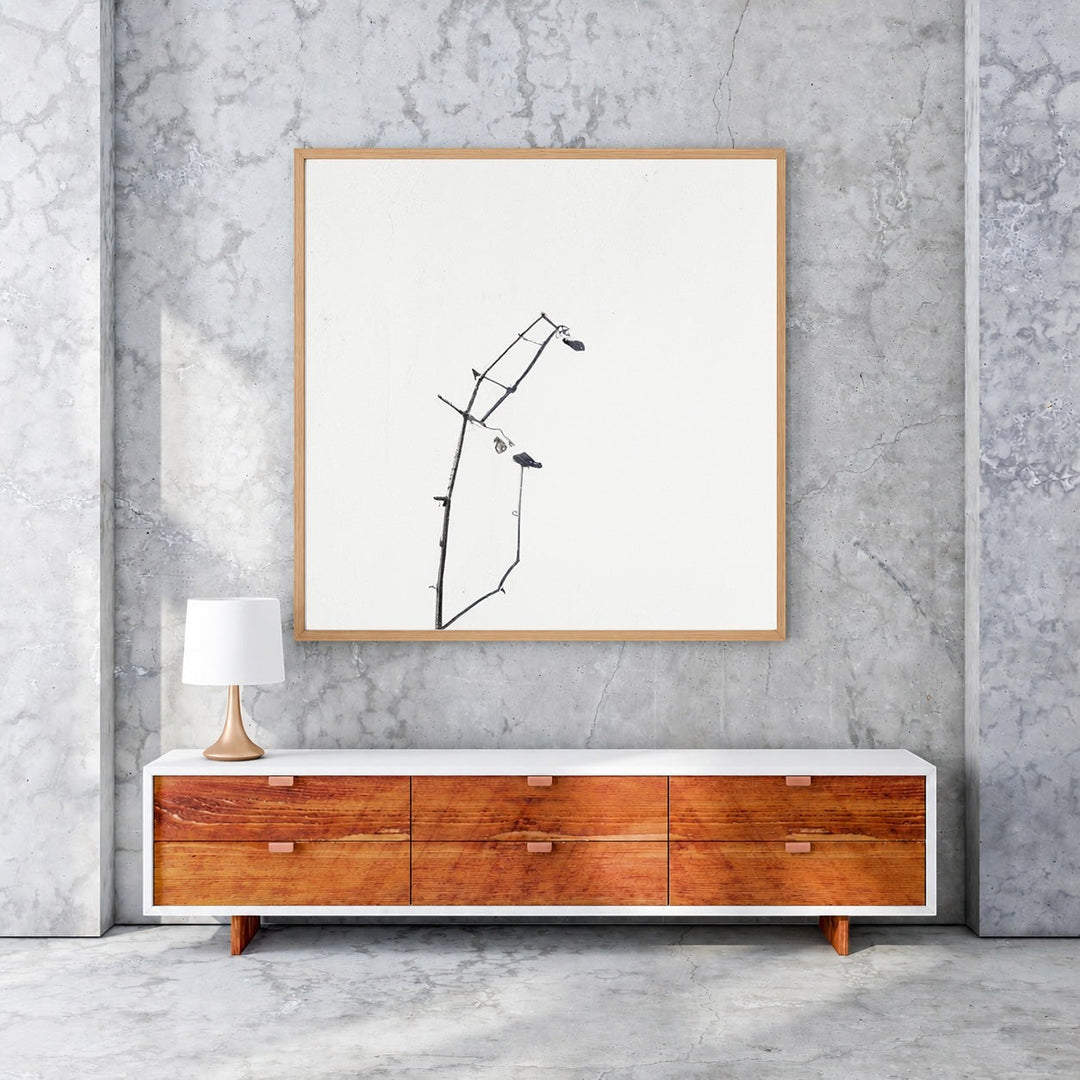 Wadi Home framed minimalist art print of dark branches on a white background, with a light wood frame.