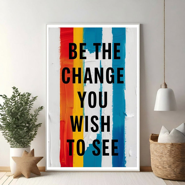 Wadi Home motivational wall art with black text 'Be The Change You Wish To See' on a background of vertical red, orange, yellow, blue, and white brushstrokes.
