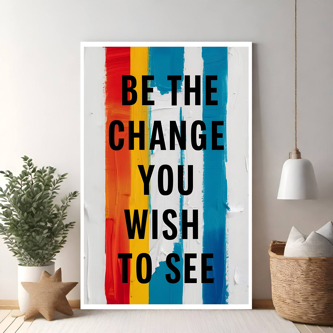 Wadi Home motivational wall art with black text "Be The Change You Wish To See" on a background of vertical red, orange, yellow, blue, and white brushstrokes.