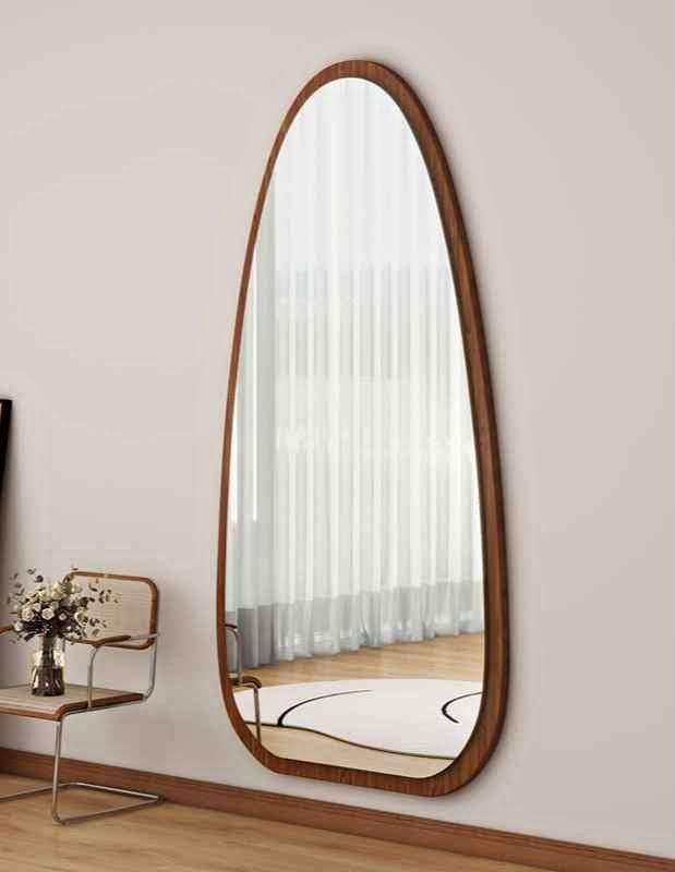 Wadi Home organic shaped full length floor mirror with a warm brown wooden frame leaning against a neutral wall.
