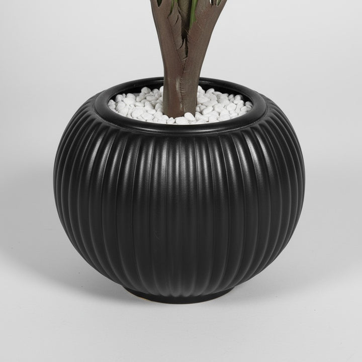 Wadi Home artificial fan palm plant in a round ribbed black ceramic-style planter topped with white decorative stones.