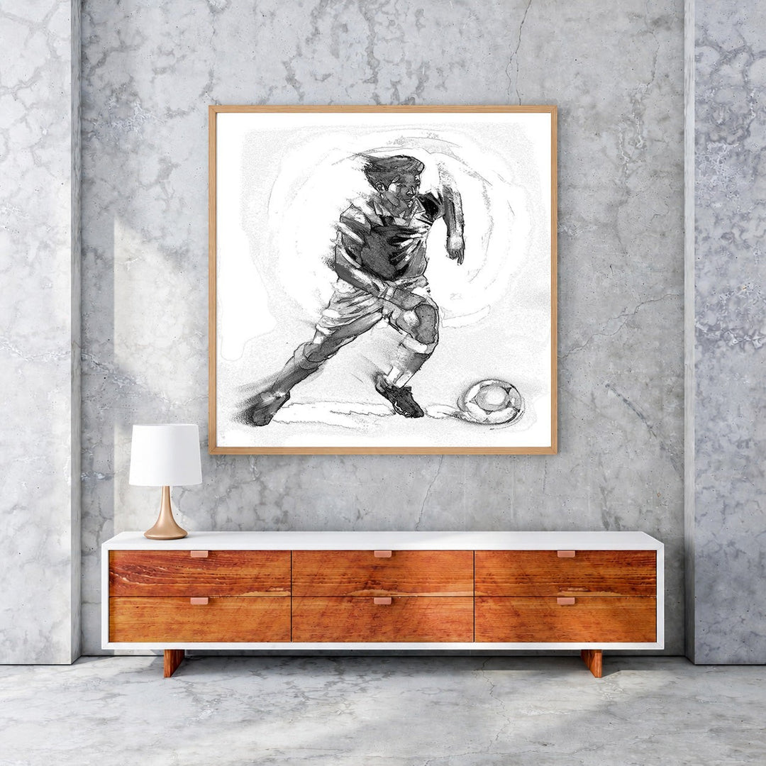 Wadi Home black and white sketch artwork of a soccer player in motion with a ball, framed in light wood.