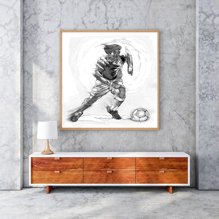 Wadi Home black and white sketch artwork of a soccer player in motion with a ball, framed in light wood.