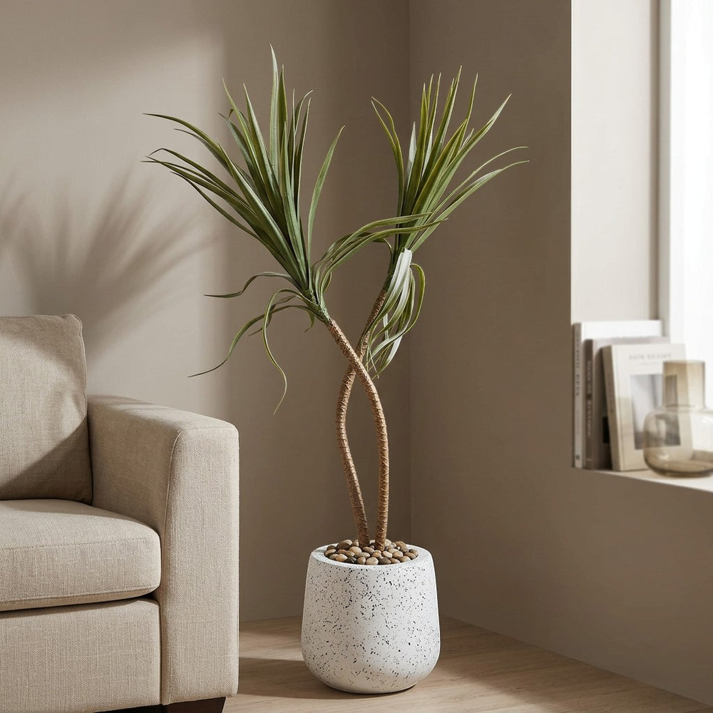 Wadi Home tall artificial plant with twisted stems and green foliage in a textured white pot with pebbles.
