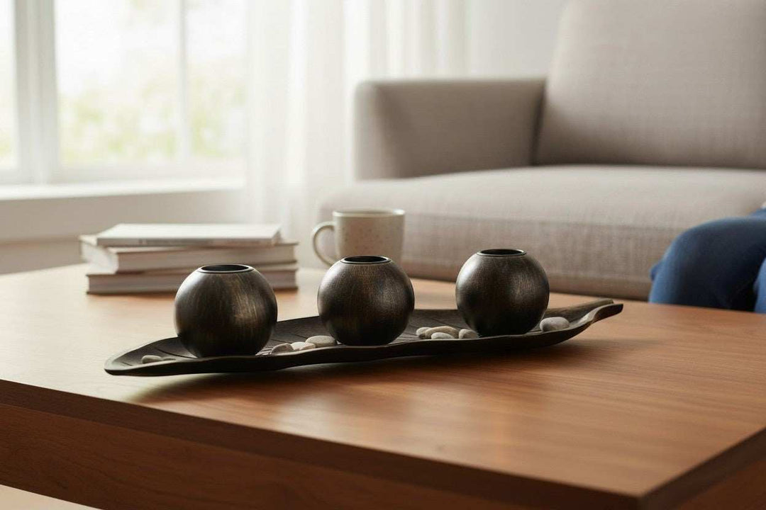 Wadi Home dark metal three sphere candle holder set on leaf tray with decorative stones.