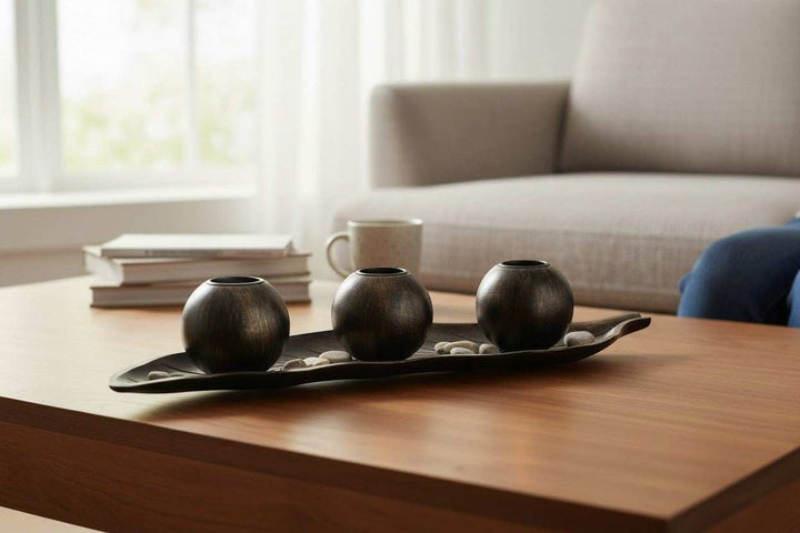 Wadi Home dark metal three sphere candle holder set on leaf tray with decorative stones.