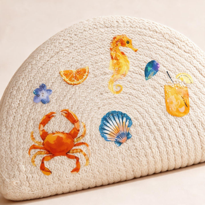 Wadi Home beige woven half moon clutch bag featuring colorful beach-themed prints of a crab, seahorse, and drinks.