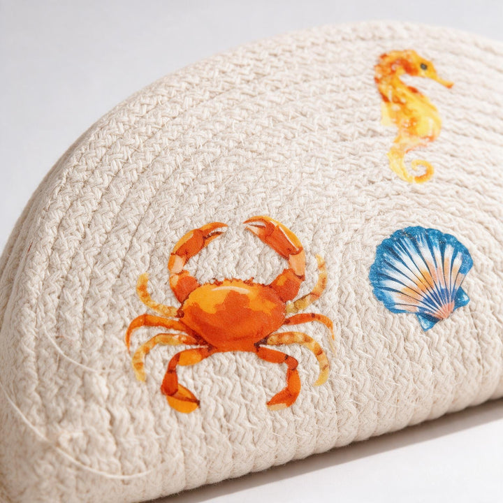 Wadi Home beige woven half moon clutch bag featuring colorful crab, seahorse, and seashell beach-themed prints.