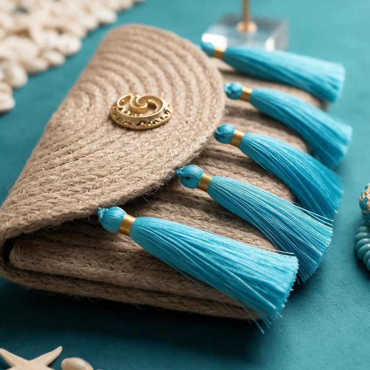 Wadi Home woven jute clutch handbag featuring turquoise tassels and a gold-tone metal accent on a teal background.