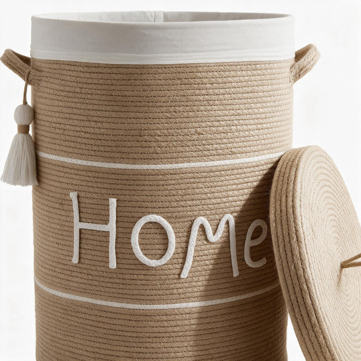 Wadi Home woven rope laundry hamper in beige with a white lid, tassel detail, and Home embroidery.