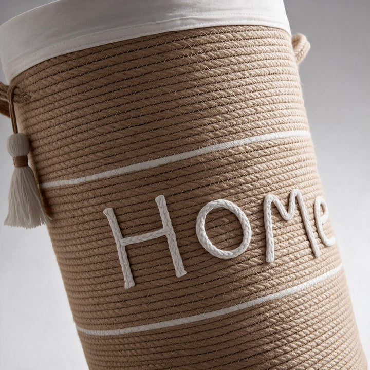 Wadi Home woven rope laundry hamper in beige with white Home text, lid, and decorative tassel detail.