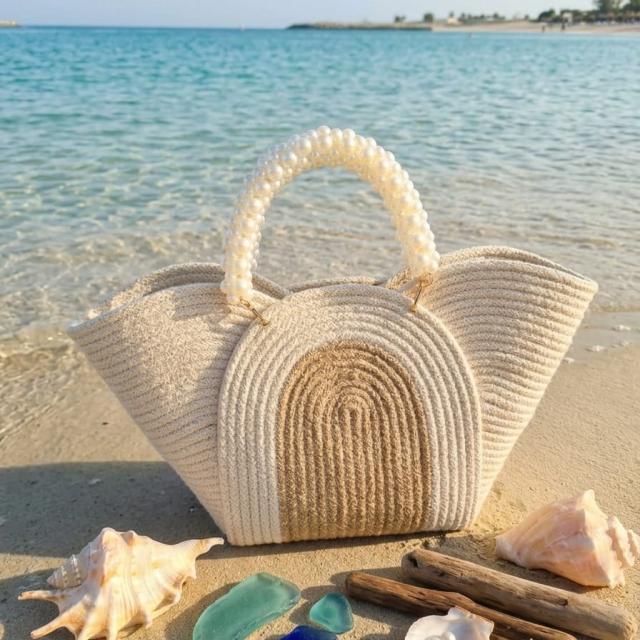 Wadi Home beige woven rope handbag with a pearl-beaded handle, displayed on a sandy beach with seashells.