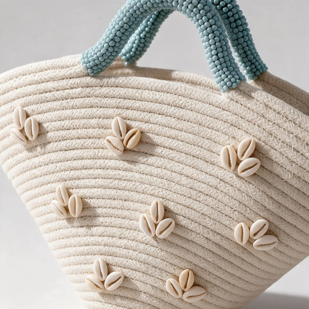 Wadi Home beige woven beach handbag with shell embellishments and light blue beaded handles in a semi-circular shape.