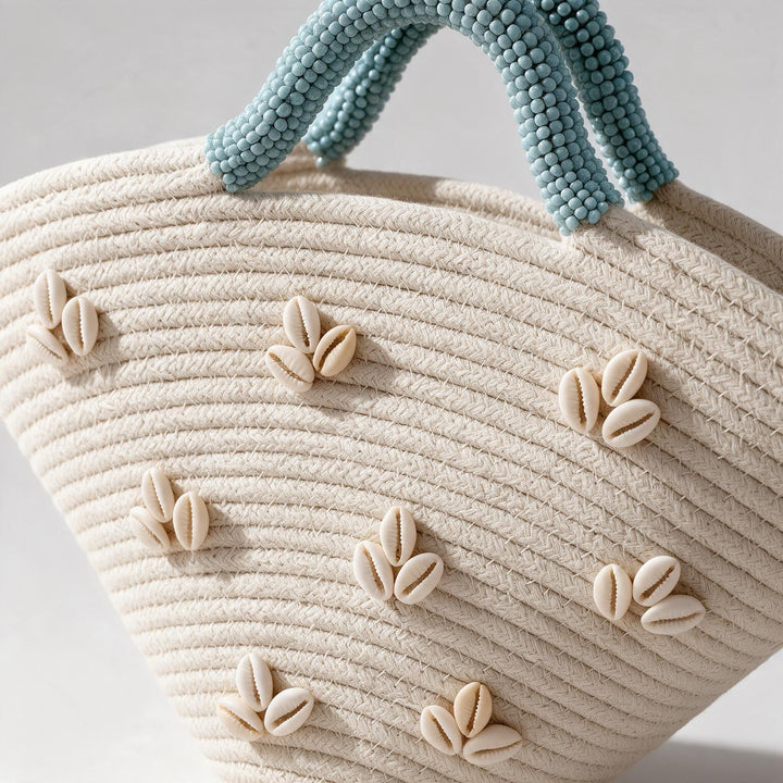 Wadi Home beige woven beach handbag with shell embellishments and light blue beaded handles in a semi-circular shape.