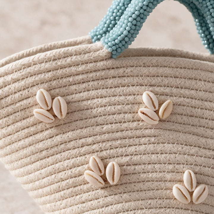 Wadi Home beige woven beach handbag featuring white shell embellishments and a textured blue beaded handle