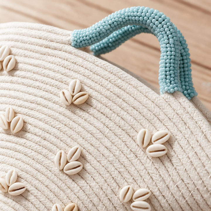 Wadi Home beige woven beach handbag featuring white shell embellishments and a textured light blue beaded handle.