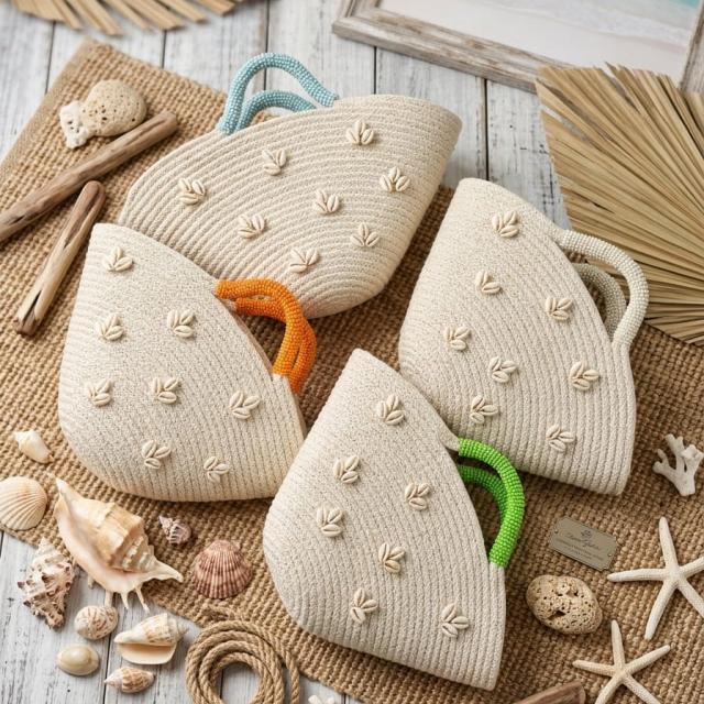 Wadi Home beige woven beach handbags with shell embellishments and colorful handles arranged on a rustic mat.
