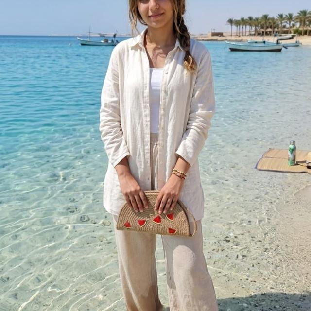 Wadi Home beige woven half moon clutch with watermelon print held by a woman on a sunny beach
