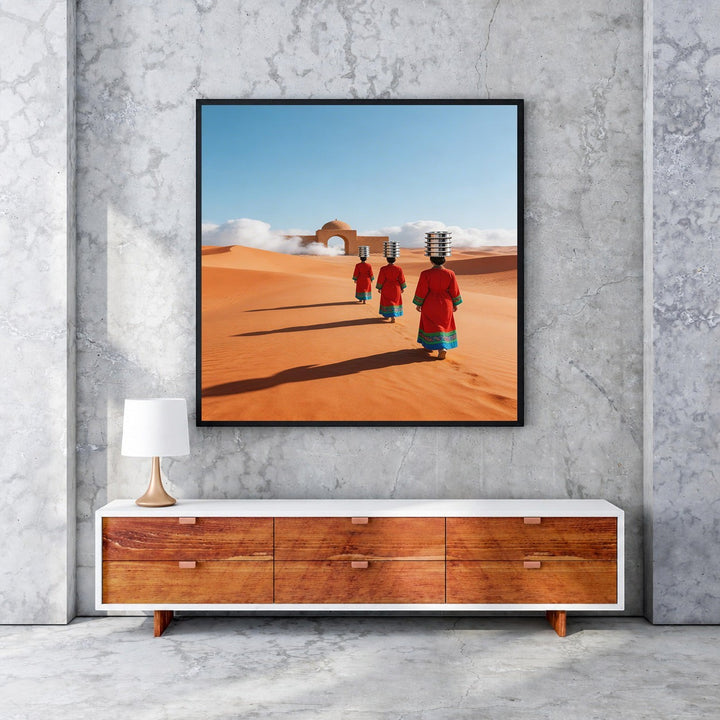 Wadi Home artwork: Three figures in red robes walk across desert dunes towards an archway, carrying items on their heads.